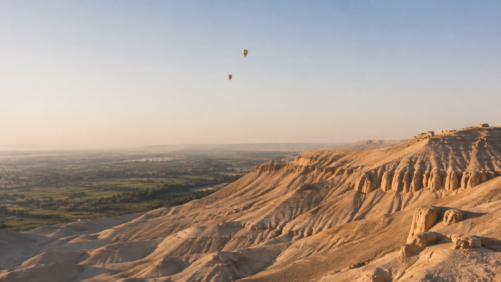 Editorial illustration: The Theban hills and cultivated Nile Valley with distant morning balloons